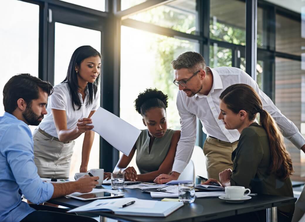 Five people working around a desk with papaers.